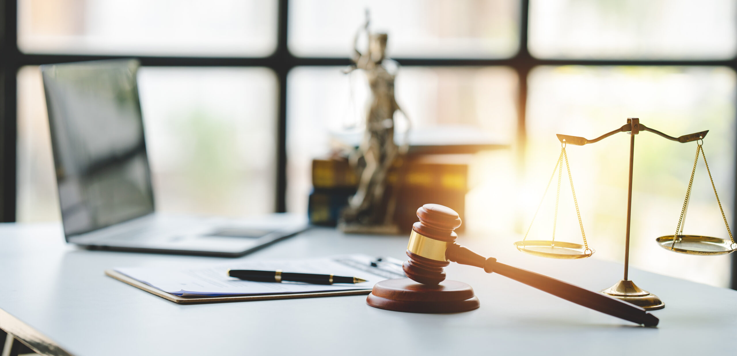 Desk with gavel, scales, statue of Lady Justice, and a laptop