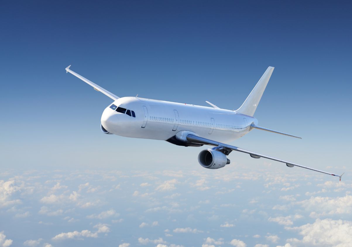 A commercial airplane with its landing gear down flies against a blue sky filled with fluffy white clouds.