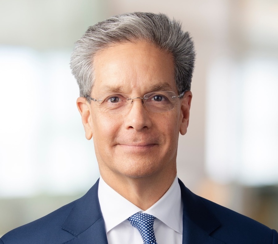 Attorney Peter Prieto wearing a navy blue suit, white shirt, and blue patterned tie, smiles slightly at the camera against a blurred background.