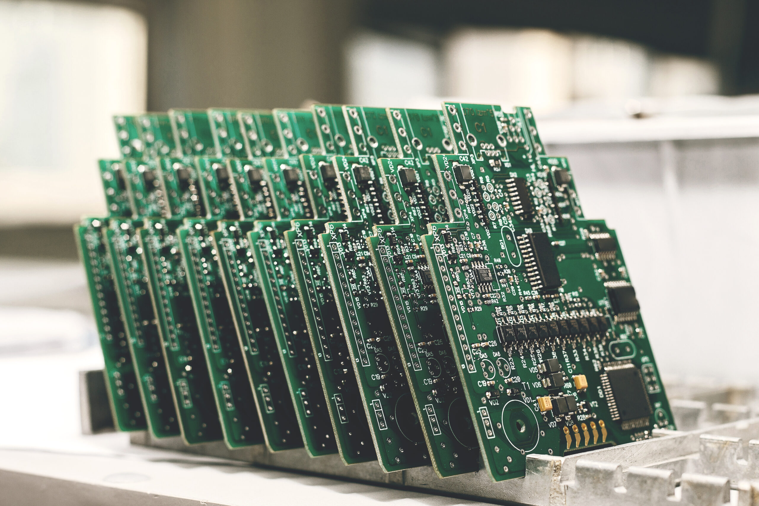 A row of green printed circuit boards (PCBs) arranged upright in a metal rack, each covered with various electronic components, inside an industrial or laboratory setting.