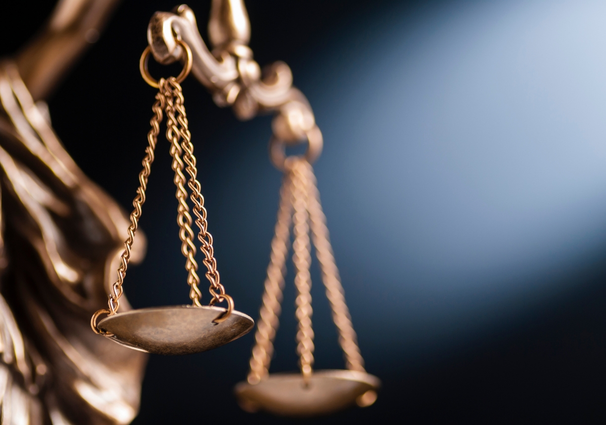 Close-up of a bronze balance scale, symbolizing justice, with a dark background and a beam of light illuminating part of the scene.